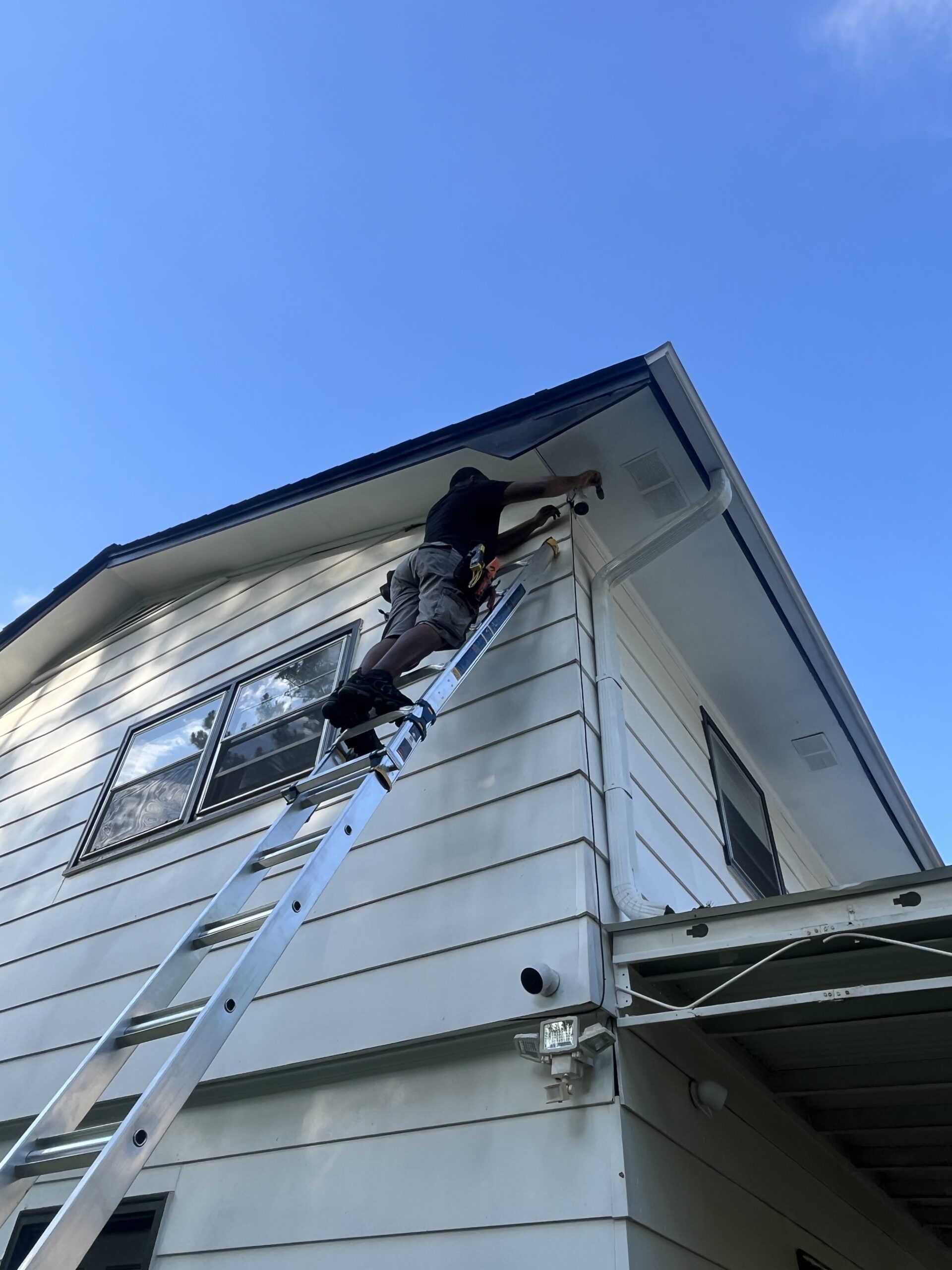 Technician on a ladder installing a camera at the corner of a house